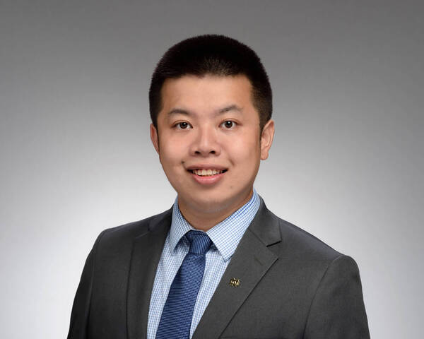 Headshot of Toby Li, A smiling man with short dark hair in a grey suit, blue checkered shirt, blue tie, and a gold Notre Dame pin on his lapel.