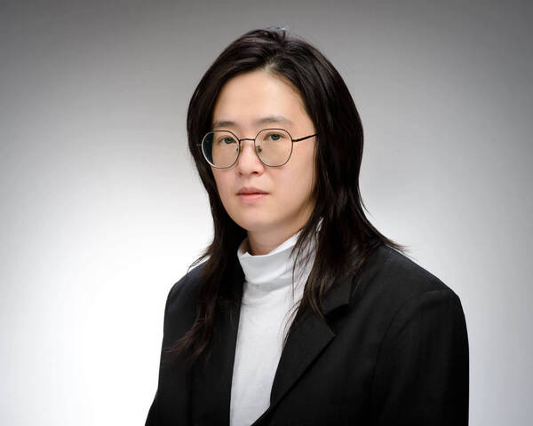 Headshot of ting Hua, a woman with long dark hair, glasses, white turtleneck, and black blazer against a gray background.