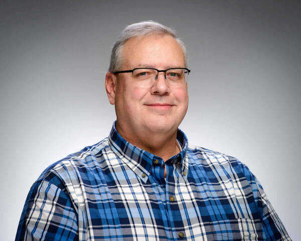 Headshot of Russ Morris, a smiling man with gray hair and glasses, wearing a blue, white, and gray plaid shirt.