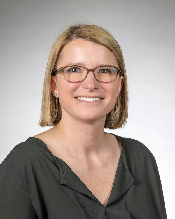 Headshot of Sarah Rucker, a blonde woman wearing glasses and a dark green top, smiling at the camera.