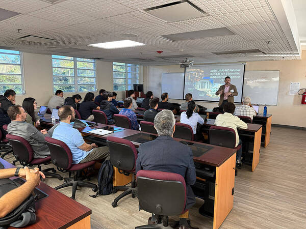 Man in a tan jacket gestures while speaking to students during the 2026 UPR-ND Winter School for Scientific Artificial Intelligence.