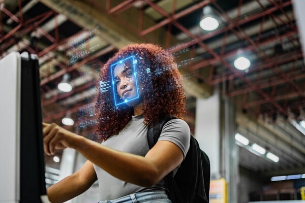 A woman with curly auburn hair interacts with a device, a blue digital overlay identifies her face.