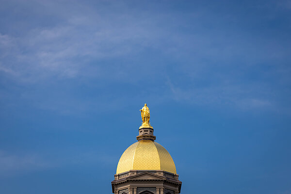 Golden dome of the Main Building topped by statue of Mary against a blue sky.